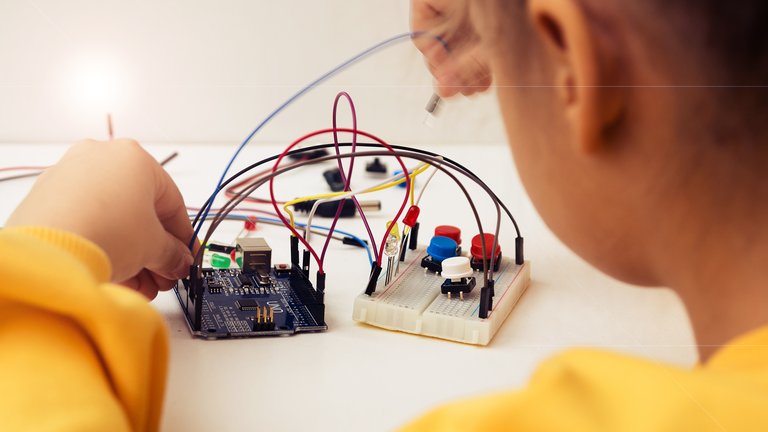 A child working with wires on a small Arduino circuit board.