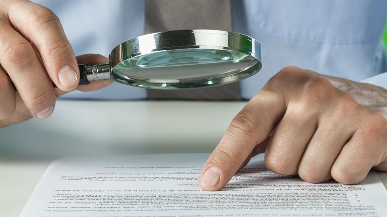 Closeup of a person reading a legal document using a magnifying glass.
