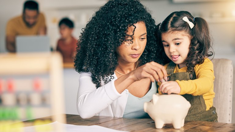 A woman and a child inserting coins in a small piggy bank