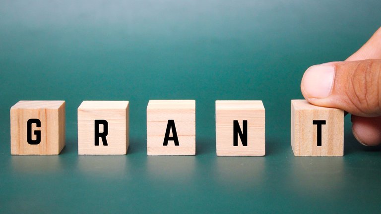 A set of wooden cubes laid side by side, each marked with a black letter that, combined, read the word Grant.