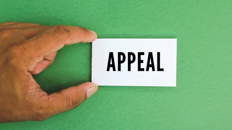 Closeup of a hand holding a small white paper that reads "Appeal" in all caps against a bright green background.