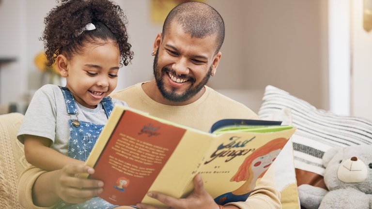 A photograph of a man with his daughter in lap reading a book