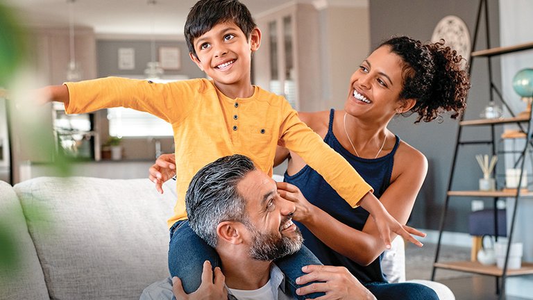 Smiling family of three playing together in a living room.