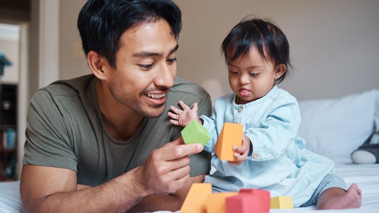 A child with down syndrome and their father playing with a geometric shapes toy set.