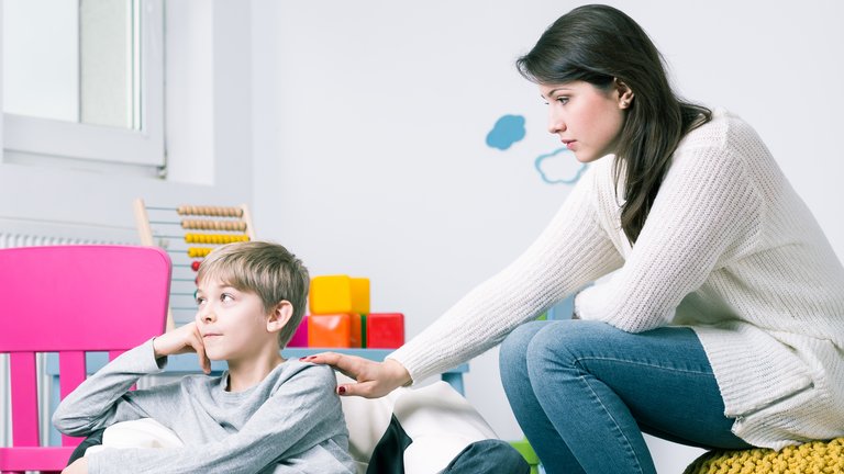 Woman comforting a sad child sitting in a playroom.