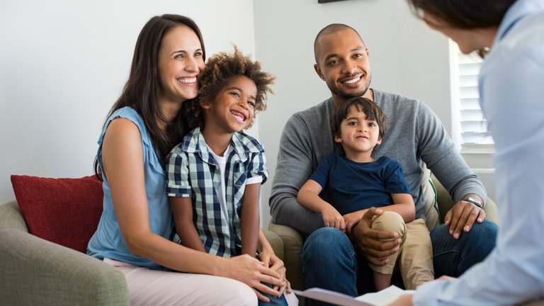A family of four sitting in armchairs and smiling in front of a social worker in a room.