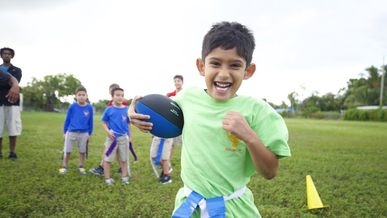 Child playing flag football outdoors, smiling.