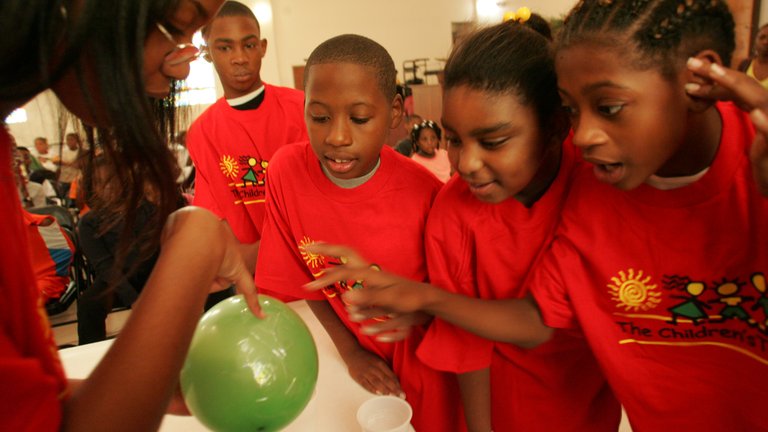Children in red shirts gathered around a green balloon.