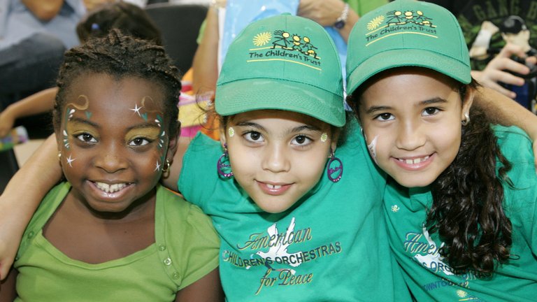 Three girls in green shirts and hats, smiling together.