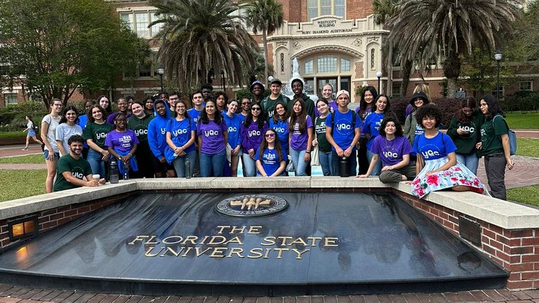 A group of people in blue and purple shirts posing in front of Florida State University emblem.