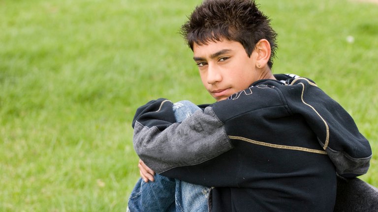 Teen boy sitting on grass, looking back with a thoughtful gaze.