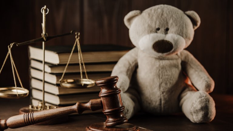 A wooden gavel, a teddy bear, a scale and a stack of books on top of a table.