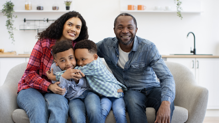 Smiling family of four sitting together on a couch at home.