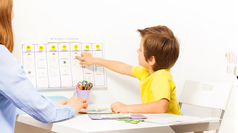 kid pointing at a calendar board with a teacher sitting next to him