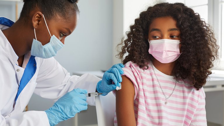 Healthcare professional administering a vaccine to a young girl wearing a mask Healthcare professional administering a vaccine to a young girl wearing a mask
