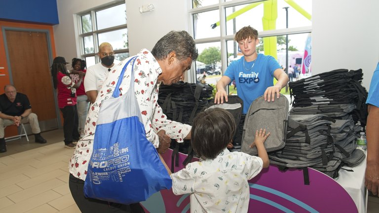 photograph of a table with free backpacks and a father with son grabbing one